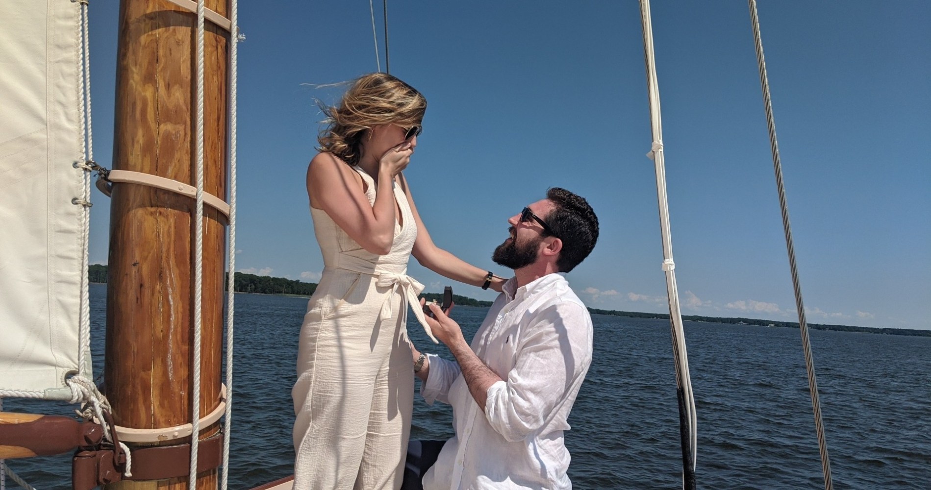 "Experience the ultimate romantic gesture with a marriage proposal on Sail Selina, the premier sailing adventure on the Chesapeake Bay in St. Michaels, MD - This heartwarming image captures the surprise and joy of a woman as her partner bends down on one knee at the bow of Sail Selina, surrounded by the stunning natural beauty of the Chesapeake Bay - With our skilled and discreet crew at your service, relish the intimate and memorable ambiance of Sail Selina's comfortable and well-maintained boat, as you create unforgettable memories that will last a lifetime - Fall in love with the timeless and romantic atmosphere of Sail Selina, perfect for intimate gatherings and unforgettable romantic experiences - Book now and discover the magic of a marriage proposal aboard Sail Selina, an experience of a lifetime that will serve as a symbol of your love for years to come.