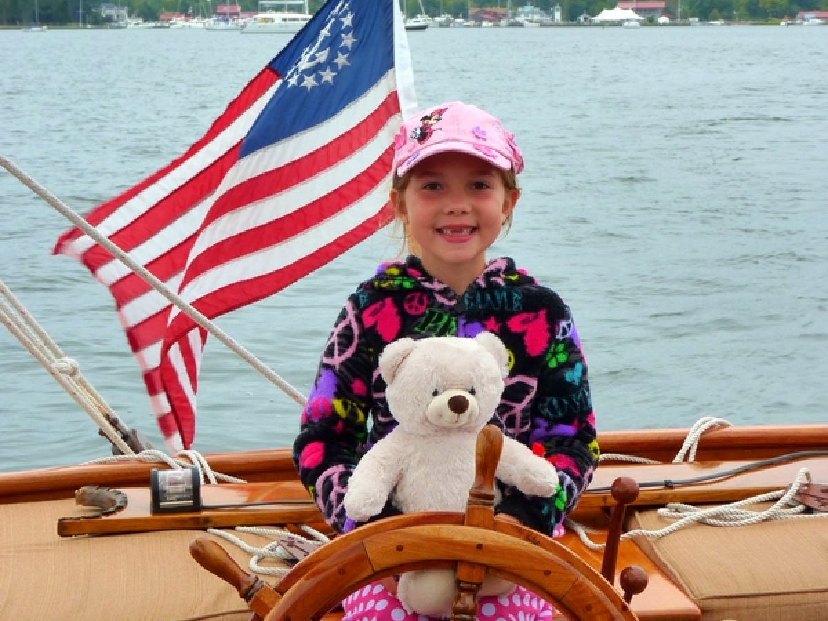 Create unforgettable family memories with Sail Selina's family-friendly sailing adventures on the Chesapeake Bay in St. Michaels, MD - This charming image captures the spirit of adventure and wonder, as a little girl and her teddy bear take the helm on Sail Selina's comfortable and well-maintained boat - With our friendly and experienced crew at your side, embark on a journey of exploration and discovery, as you marvel at the beauty of the open waters - Fall in love with Sail Selina's warm and welcoming atmosphere, perfect for family vacations and outdoor adventures - Book now and give your family the gift of a lifetime, a unique and meaningful Sail Selina family sailing adventure!