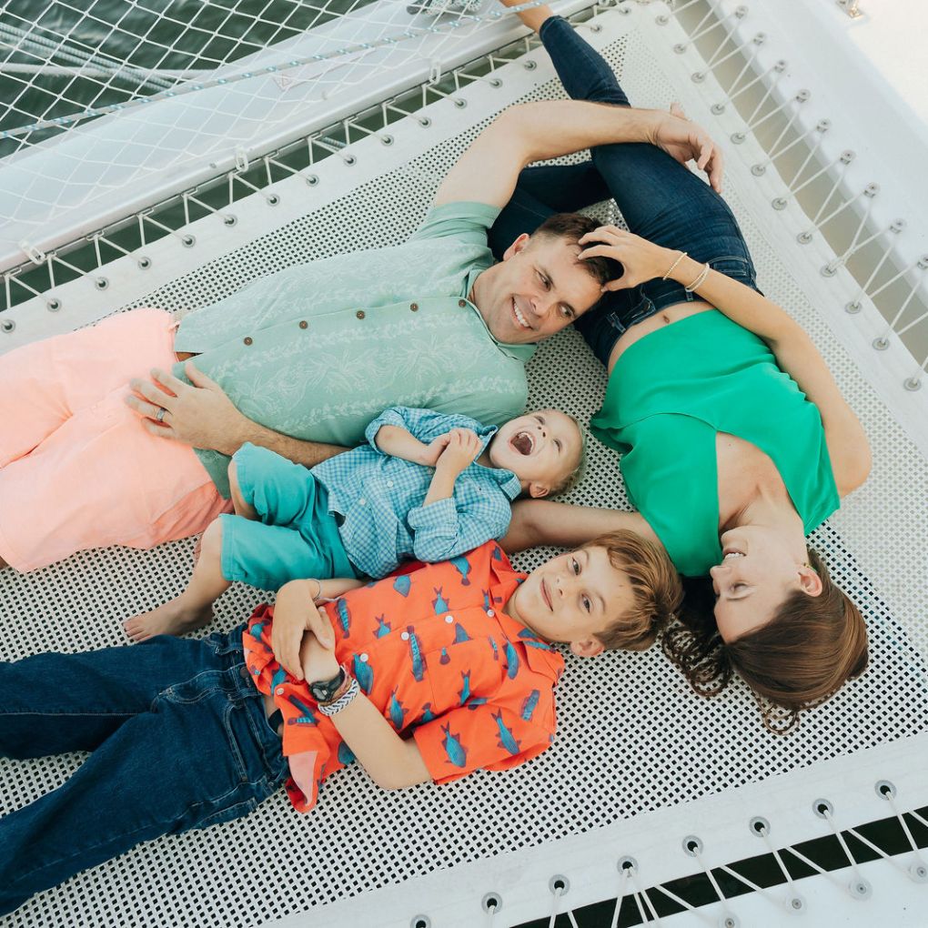 Family of four lying on a netted platform, smiling and enjoying a relaxed moment.